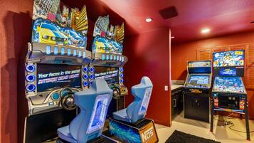 A gaming area with multiple arcade machines, including racing and golf games, and two racing game chairs.