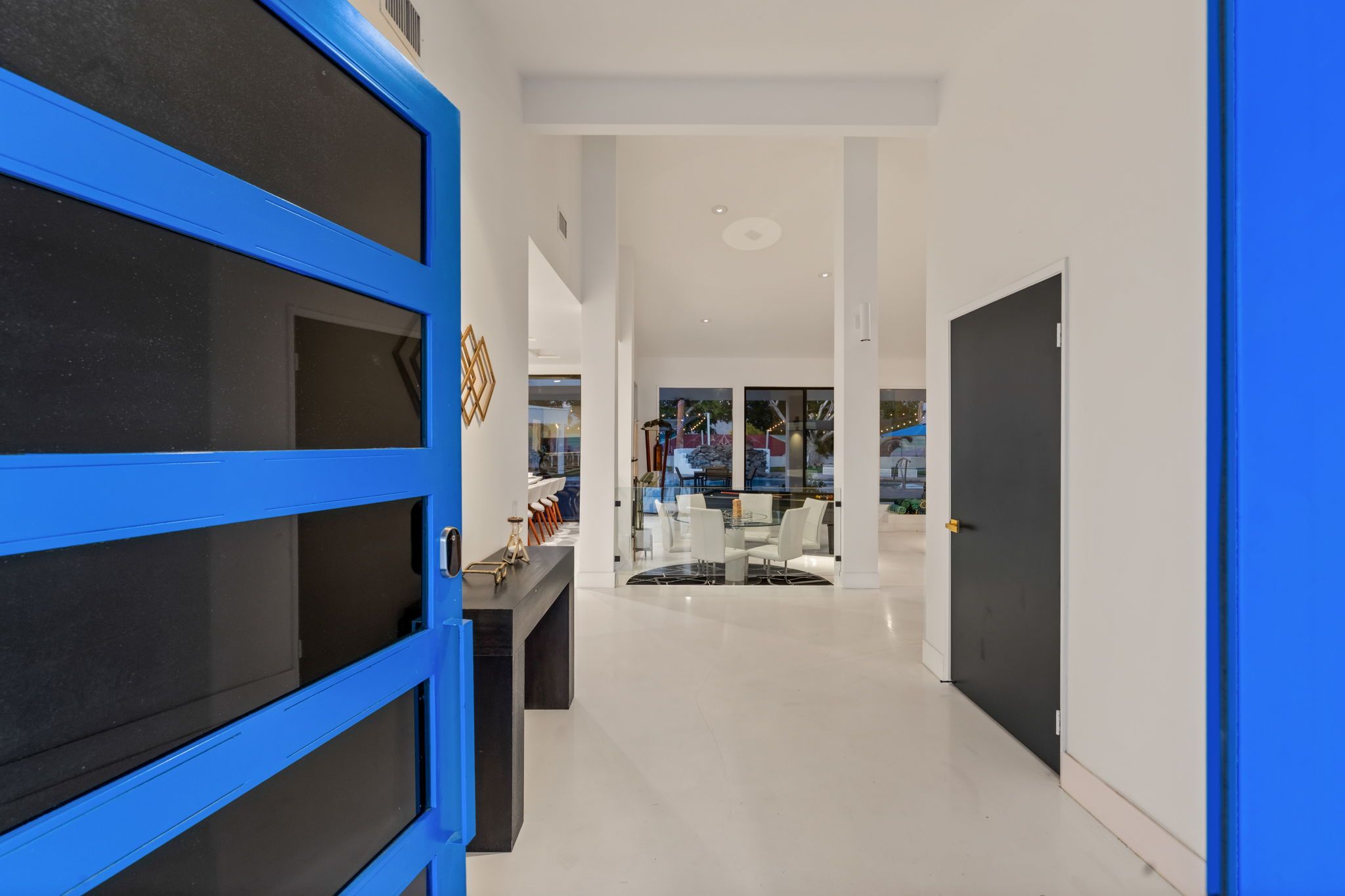A modern interior with a blue door, a glass partition, and a dining area with white chairs.