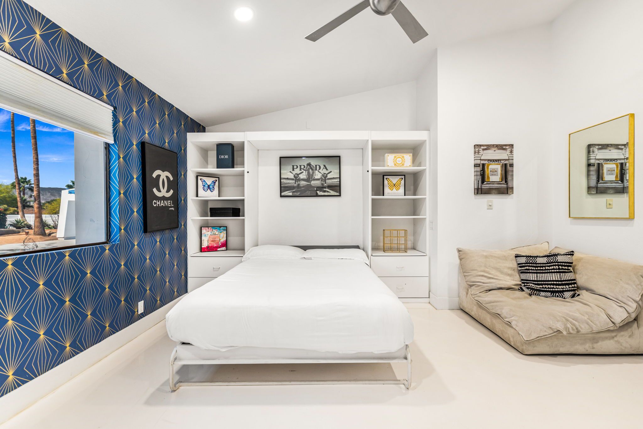 A bedroom with a bed, a sofa, a wall with a geometric pattern, and a ceiling fan.