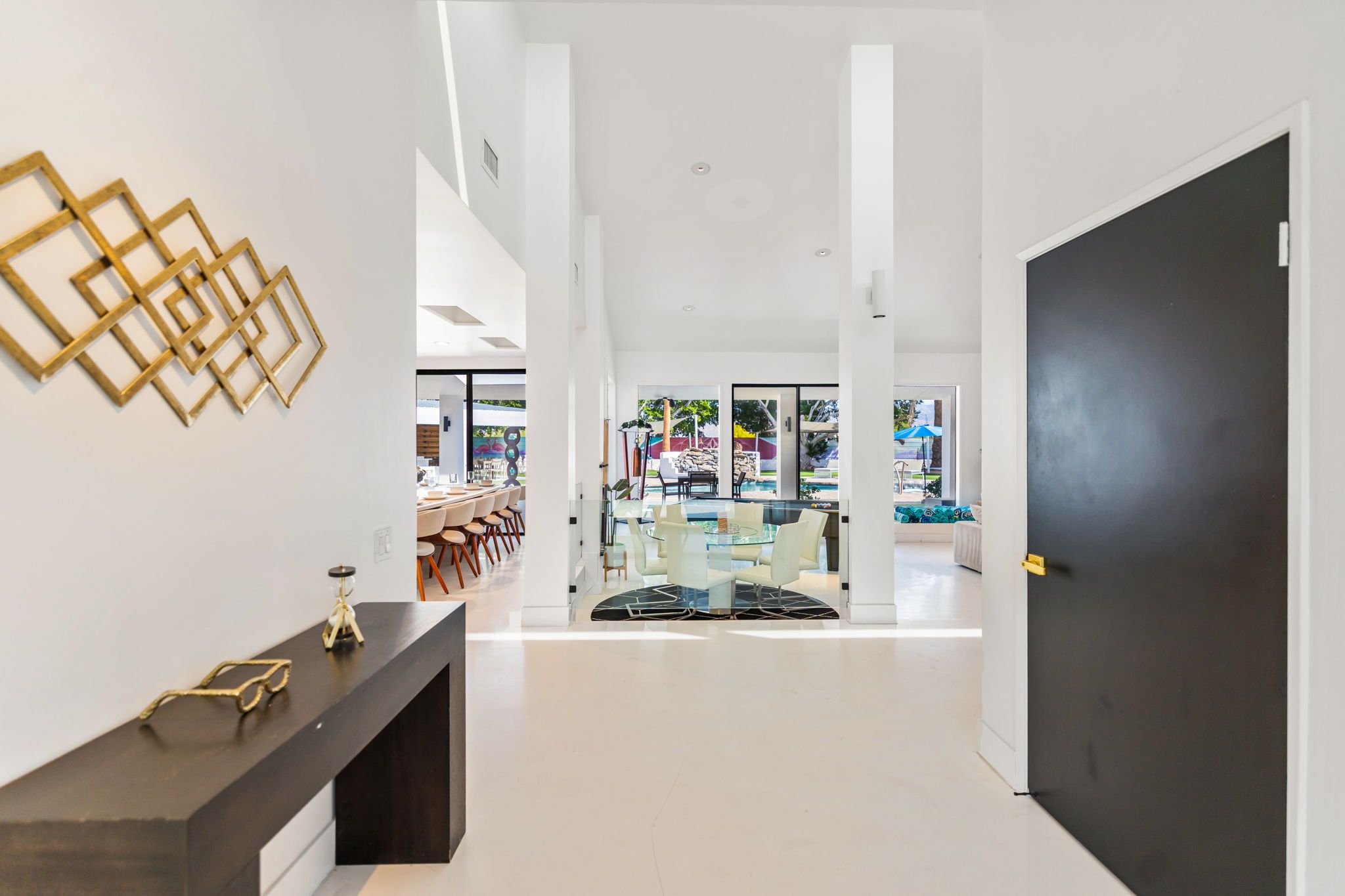 Un interior moderno con un mostrador de recepción de tonos oscuros, una obra de arte mural geométrica y vistas a una zona de comedor exterior con sillas y una piscina.