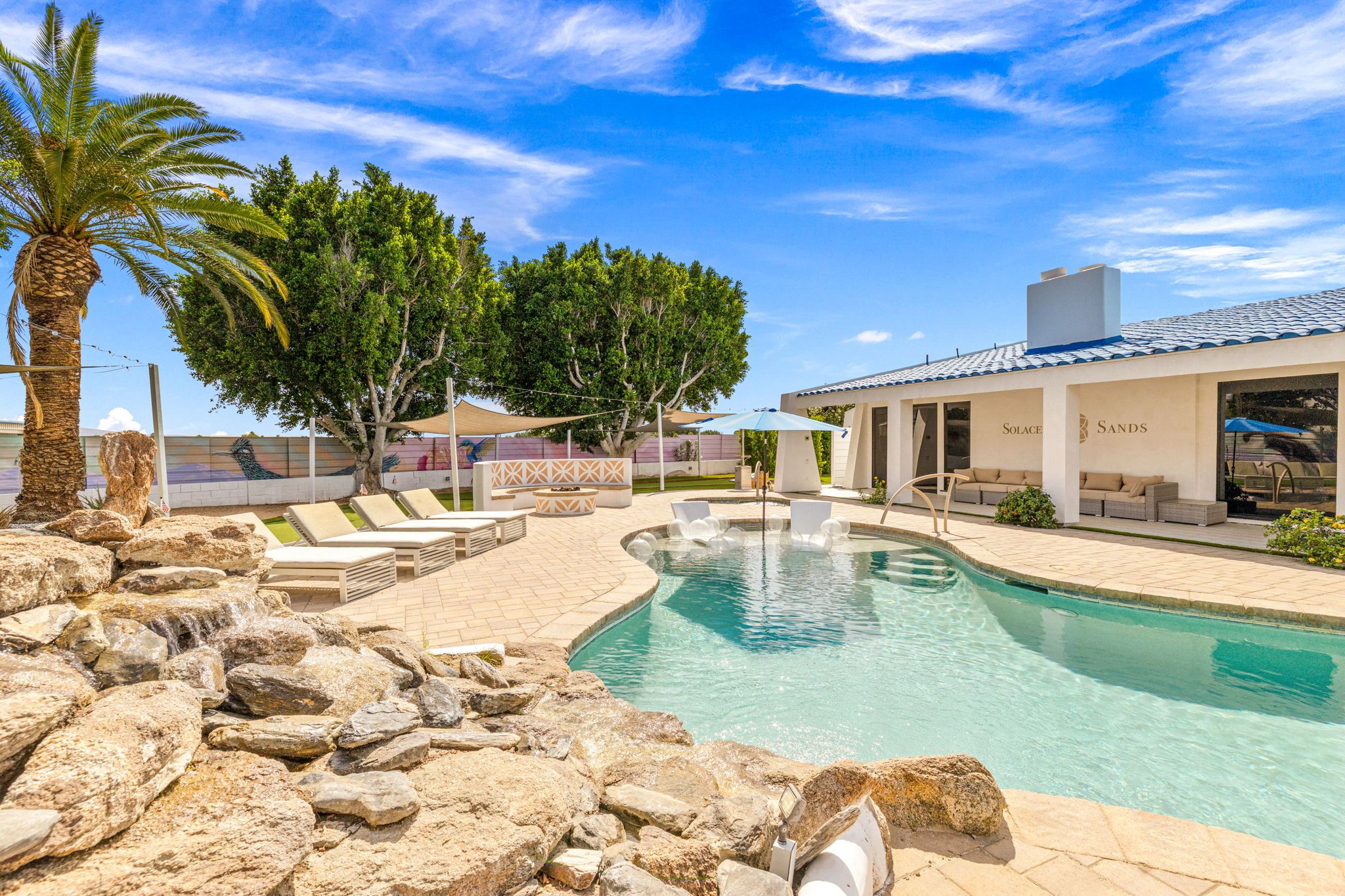 A pool area with lounge chairs, a fountain, and a building with the name 'Solsace Sands'.