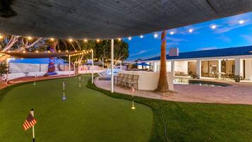 A well-lit outdoor area with artificial turf, a pool, and a covered seating area.