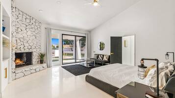 A modern bedroom with a stone fireplace, a bed, a desk, and a view to an outdoor patio.