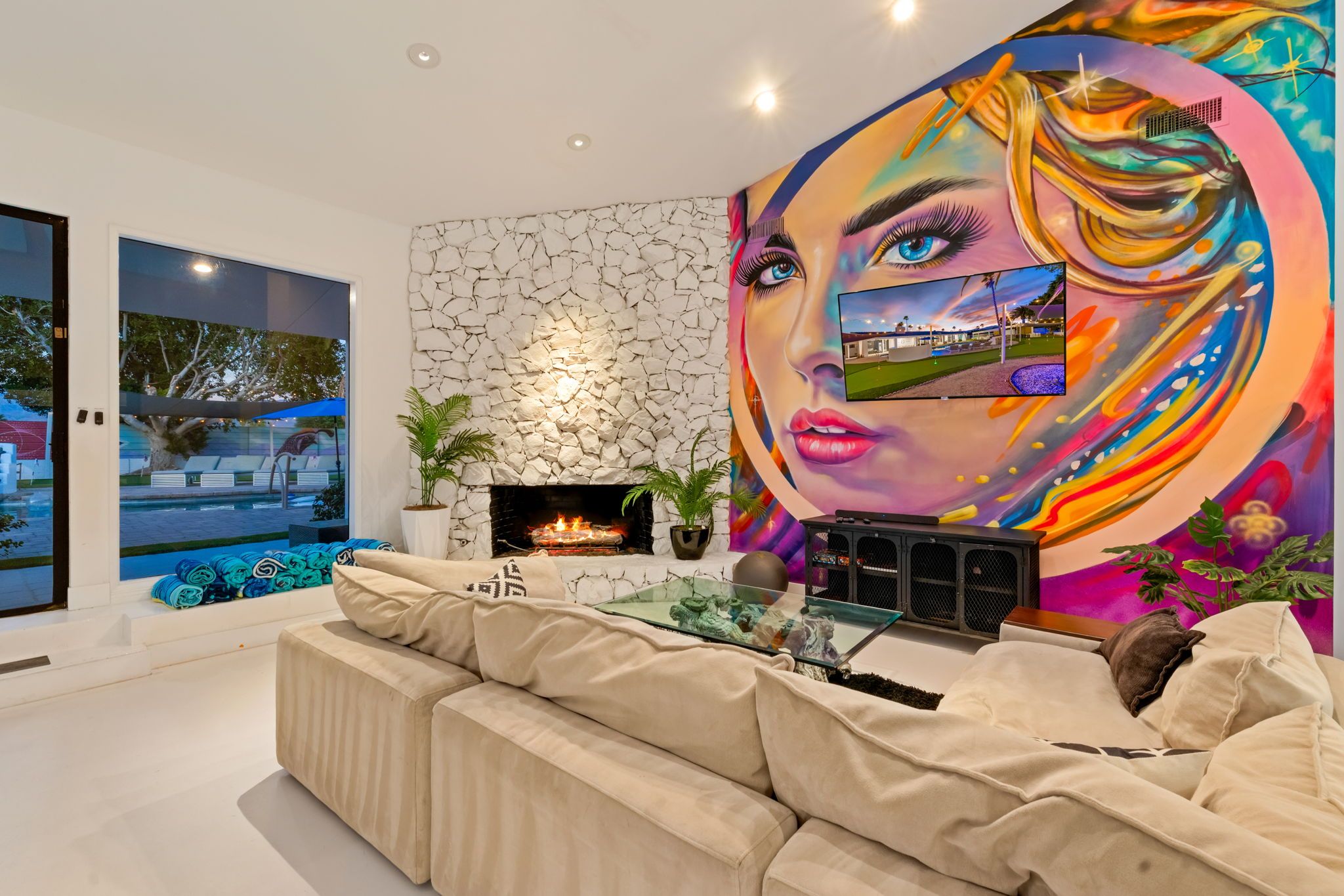 Una sala de estar moderna con chimenea de piedra, televisor grande y un mural colorido.