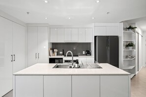 Eine moderne Küche mit weißen Schränken, einer zentralen Kochinsel mit Spüle, einem eingebauten Ofen und einem schwarzen Kühlschrank.