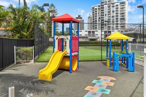 A playground with a yellow slide, climbing structures, and a fenced area. - Fern Escape Resort Living near Beach and Nightlife (Gold Coast)