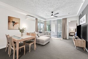 Ein modernes Hotelzimmer mit Essbereich, einer Couch, einem Fernseher und einem Balkon mit Vorhängen.