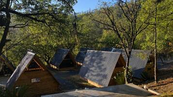 Un camping con varias cabañas de madera, algunas con techo de metal, rodeado de árboles y un cielo despejado.