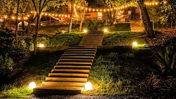 A nighttime outdoor pathway with steps leading to a building, surrounded by trees and illuminated by string lights.