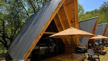 Une cabane en bois avec un toit en pente, un espace extérieur aménagé pour s’asseoir et un barbecue.