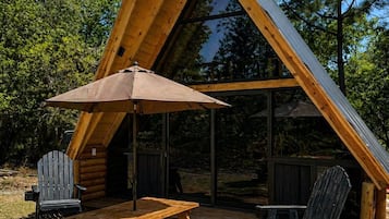 A triangular wooden cabin with a picnic table and chairs, a grill, and a covered seating area.