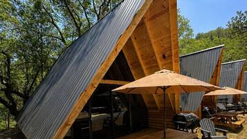 Une cabane en bois avec un toit en pente, un espace extérieur aménagé pour s’asseoir et un barbecue.