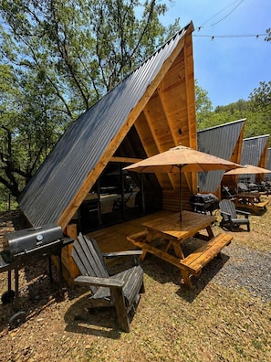 Eine Holzhütte mit geneigtem Dach, Sitzgelegenheit im Freien und einem Grill.