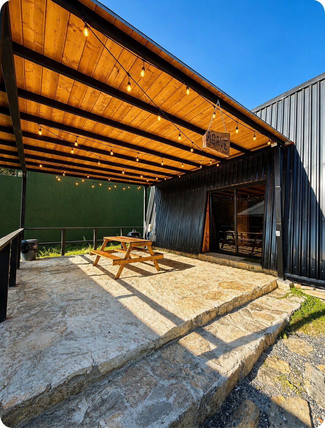 An outdoor patio with a wooden deck, a hanging sign, and a stone floor.