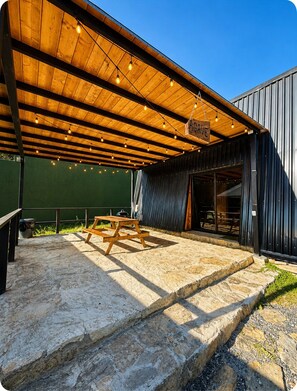 An outdoor patio with a wooden deck, a hanging sign, and a stone floor. - VILLA AMADA. Cabaña Agave (Santiago)
