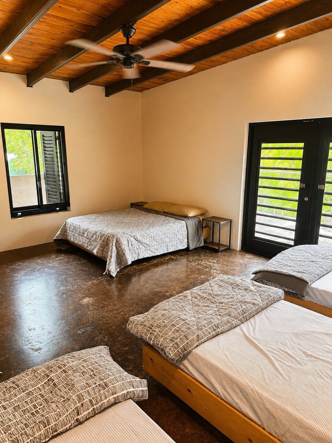 A room with three beds, a ceiling fan, and a window with blinds.