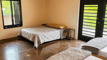 A room with three beds, a ceiling fan, and a window with blinds.