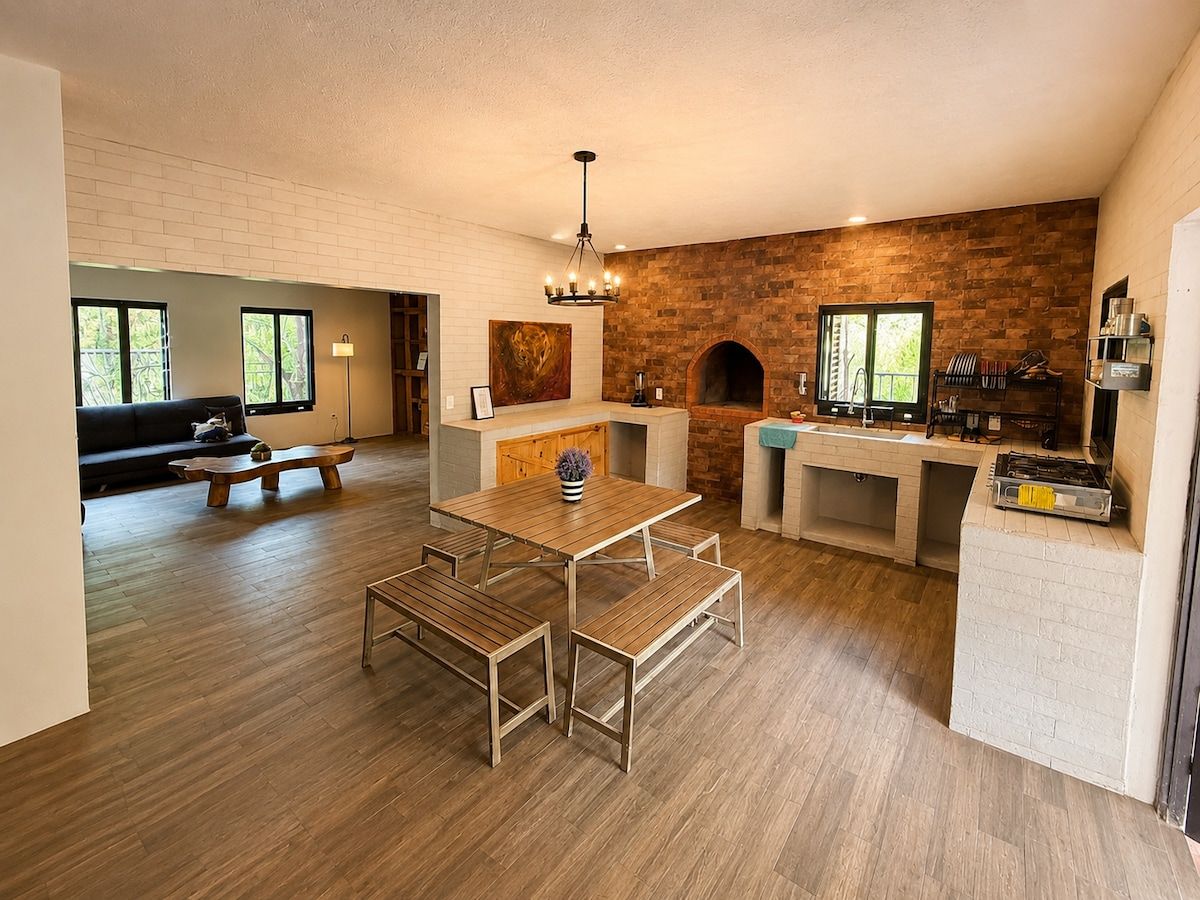 A modern kitchen with a brick wall, wooden flooring, a dining area with benches, and a built-in grill.
