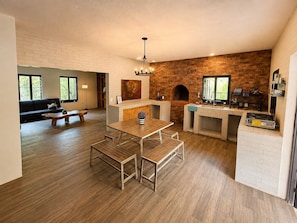 A modern kitchen with a brick wall, wooden flooring, a dining area with benches, and a built-in grill.