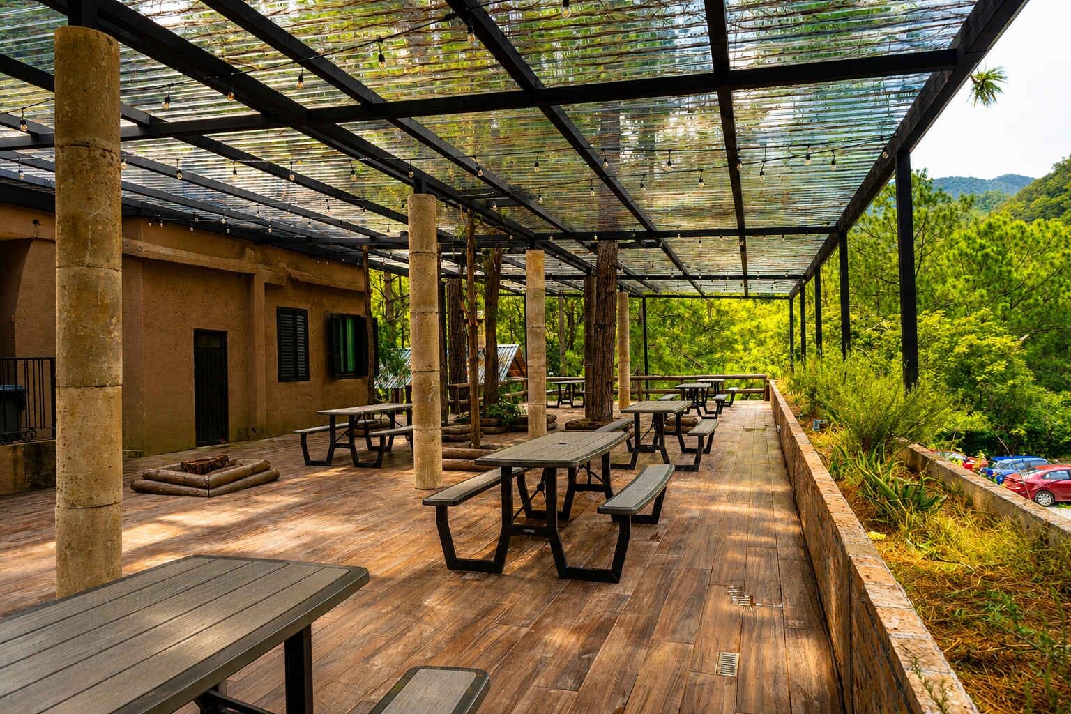 Zona de pati exterior coberta amb taules i bancs de fusta, envoltada de vegetació i vistes al paisatge.