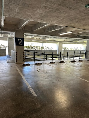 Eine überdachte Parkgarage mit Betonpfeilern, Metallgeländern und feuchtem Boden.