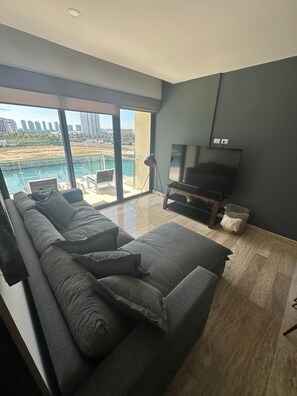 A modern living room with a large window, a flat-screen TV, a sofa, and a small table. - El Encuentro. Espectacular para viaje y descanso. (Cancún)
