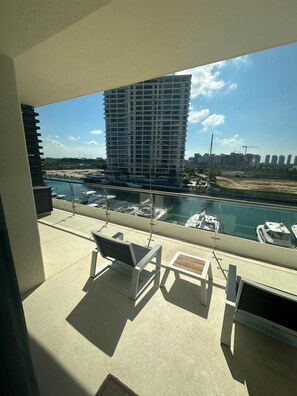 A balcony with a view of a marina, a tall building, and a clear sky. - El Encuentro. Espectacular para viaje y descanso. (Cancún)
