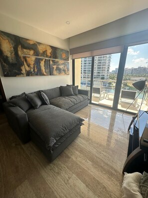 Ein modernes Wohnzimmer mit einer Eckcouch, großen Fenstern und Blick auf die Stadt.