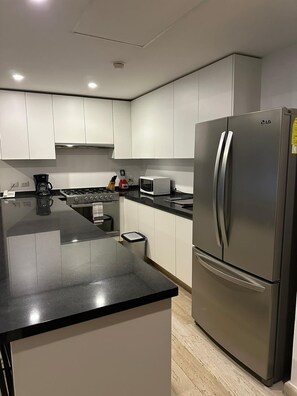 Une cuisine moderne dotée d’appareils électroménagers en acier inoxydable, de meubles blancs et d’un plan de travail noir.