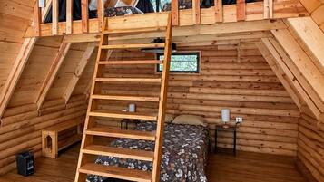 A wooden loft bedroom with a wooden ladder, a bed, and a small table.