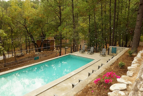 Una piscina rectangular envoltada per una taronja de pedra, amb una coberta de fusta i cadires a prop.