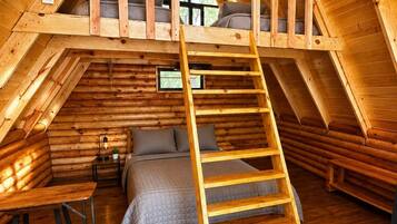 Eine Blockhütte mit Schlafzimmer auf der oberen Etage, einer Holzleiter und einem Bett mit gesteppter Decke.