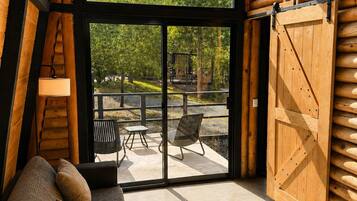 Interior moderno de cabaña de troncos con un sofá, un pouf tejido y vistas a un patio con mobiliario exterior.