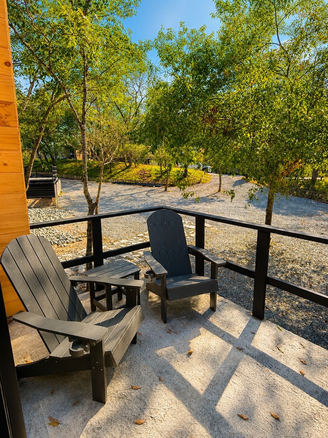 A wooden deck with two Adirondack chairs and a small table, surrounded by a metal railing.