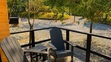 A wooden deck with two Adirondack chairs and a small table, surrounded by a metal railing.