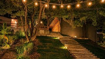 Ein Außenbereich bei Nacht mit einer Steintreppe, die zu einem Gebäude führt, umgeben von Bäumen und Lichterketten.