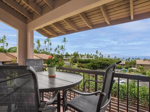 A covered outdoor seating area with a table and chairs, overlooking a residential neighborhood with palm trees and houses. - Wailea Ekahi Village 17D (Wailea)