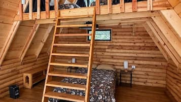 A wooden loft bedroom with a wooden ladder, a bed, and a small table.