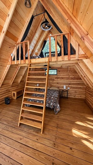 A wooden loft bedroom with a wooden ladder, a bed, and a small table.