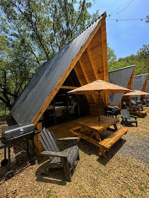 Eine Holzhütte mit geneigtem Dach, Sitzgelegenheit im Freien und einem Grill.