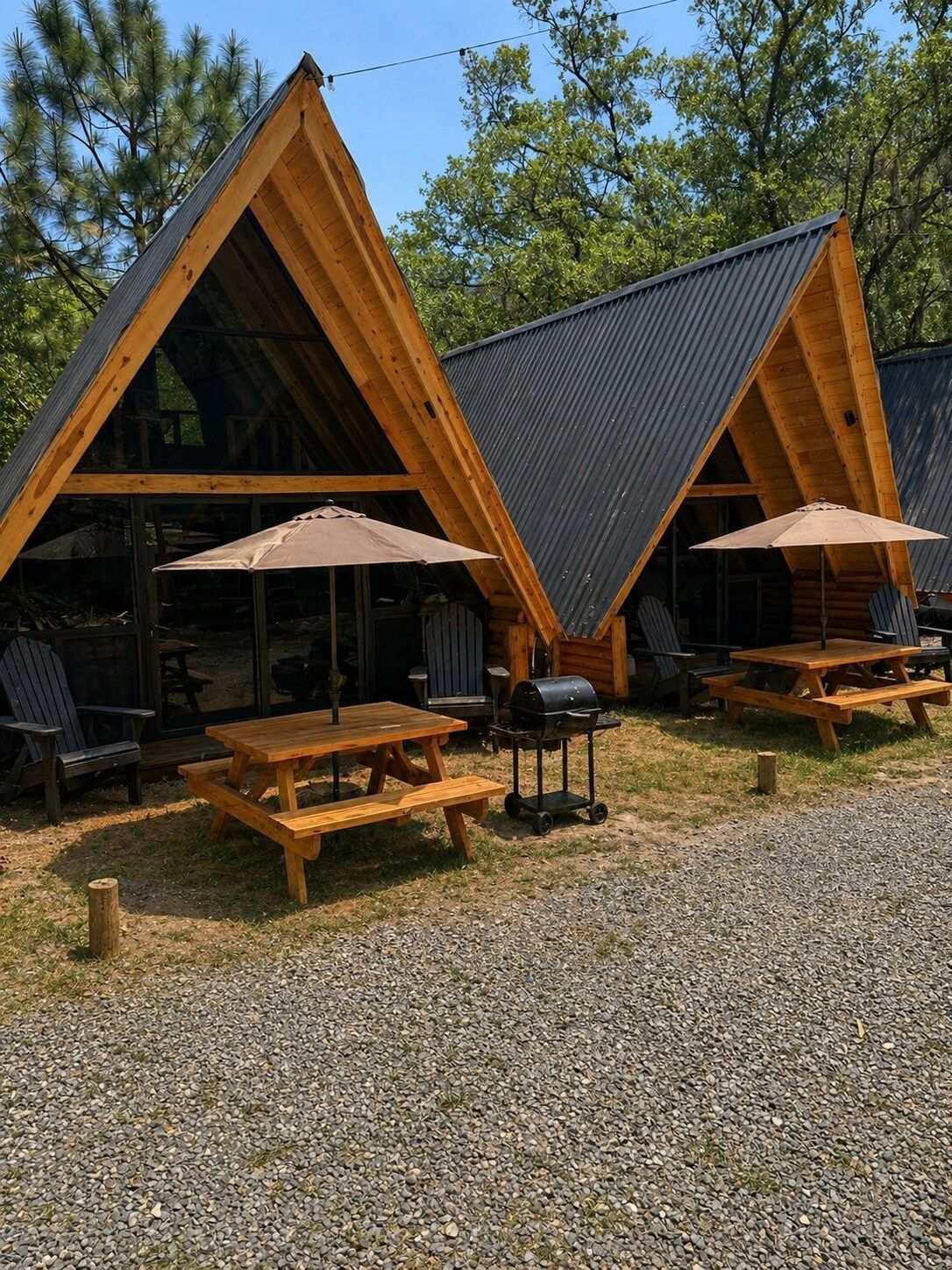 Deux cabanes en bois avec des toits à deux versants, chacune étant équipée d’une table de pique-nique et d’un parasol.