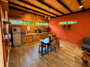 A wooden cabin interior with a dining area, kitchen, and a red wall.