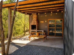 An outdoor patio with a stone fireplace, wooden bench, and string lights. - VILLA AMADA. Cabaña Abejas. (Santiago)