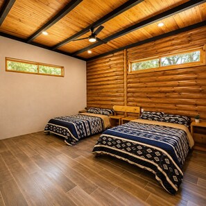 A room with two beds, wooden ceiling beams, and a window with a view of trees.