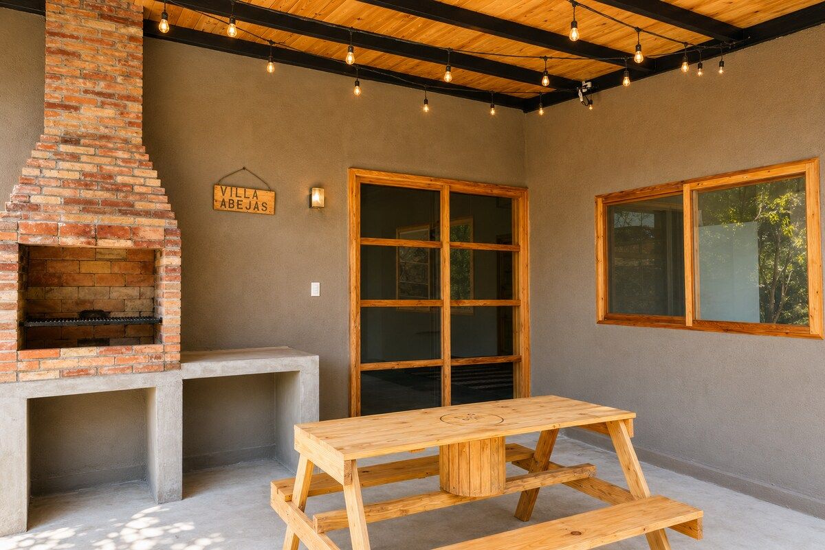 An outdoor patio with a brick fireplace, a wooden table, and large windows.