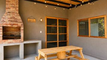 An outdoor patio with a brick fireplace, a wooden table, and large windows.