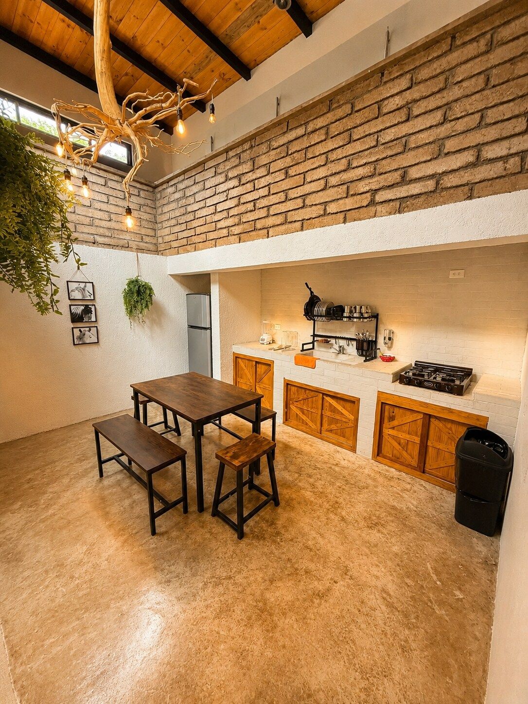 A rustic kitchen with a brick wall, wooden cabinets, and a dining area with a table and benches.