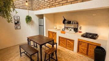 A rustic kitchen with a brick wall, wooden cabinets, and a dining area with a table and benches.