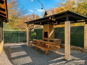 A covered outdoor seating area with a grill, wooden picnic table, and string lights.