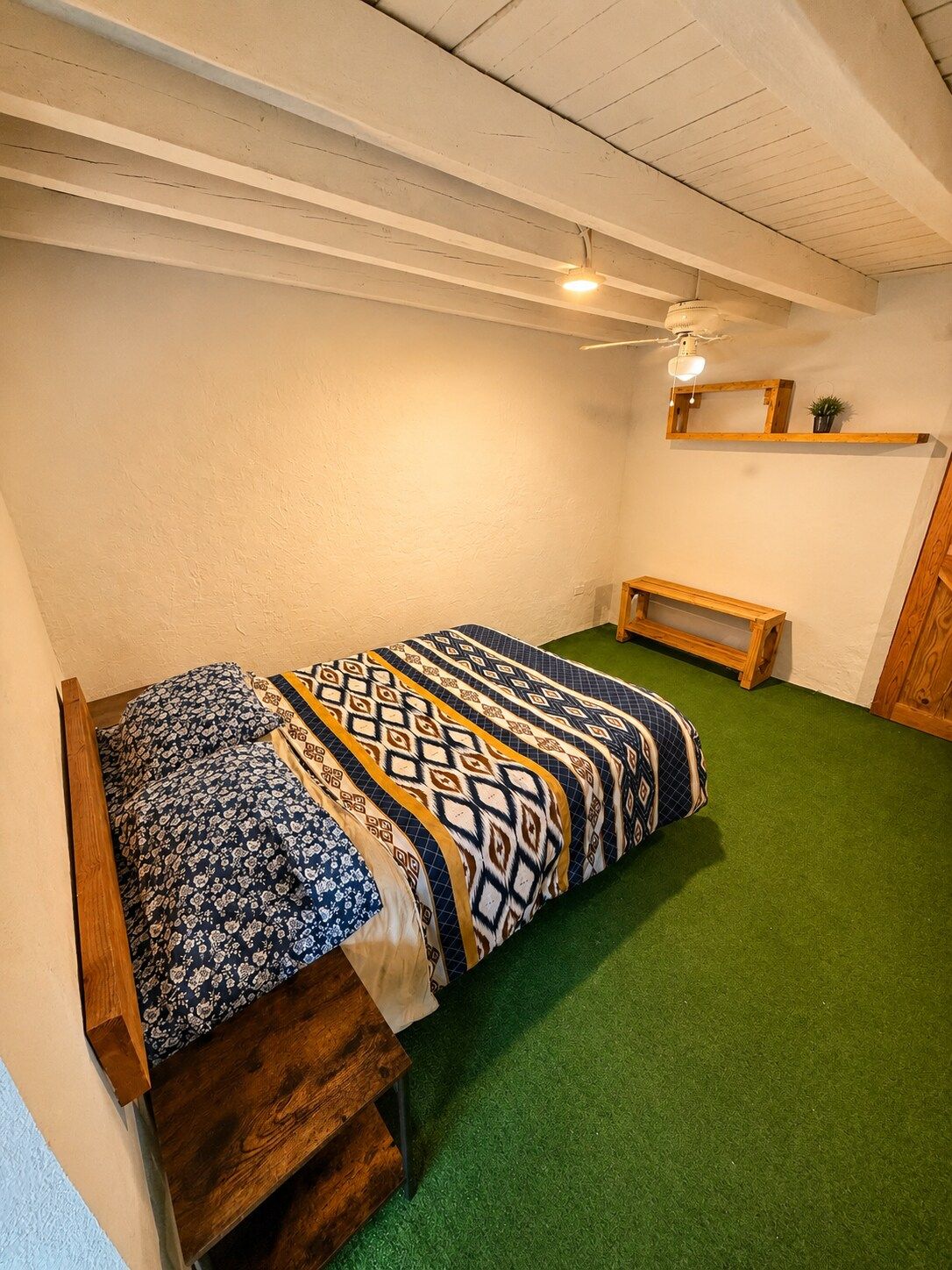 A small, cozy room with a single bed, a wooden bench, and a ceiling fan.